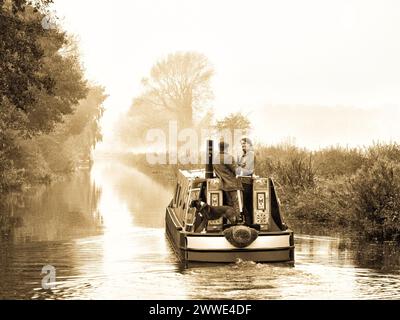 Couple et leur chien naviguent l'hiver sur leur bateau étroit sur le canal Trent et Mersey, Angleterre, Royaume-Uni, Grande-Bretagne près d'Alrewas, Staffordshire Banque D'Images