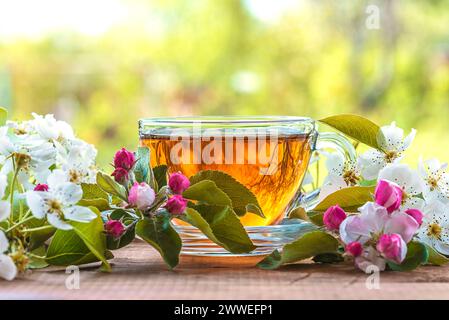 Tasse de verre de thé et fleur de pomme sur une table à l'extérieur Banque D'Images