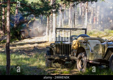 Reconstitution historique. Deux véhicules militaires américains abandonnés se tiennent dans la forêt sur le champ de bataille dans la poussière et la fumée après une explosion d'obus Banque D'Images