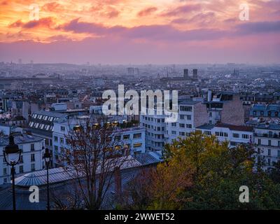 Vue sur Paris depuis le Sacré-Cœur à Montmartre au coucher du soleil, avec les toits de la ville, les arbres d'automne et le ciel rose spectaculaire du soir au-dessus de la capitale française Banque D'Images