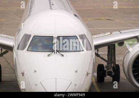 Vue de face d'un avion de ligne moderne blanc avec gros plan des fenêtres du cockpit. L'avion est assis sur un tarmac en béton avec des lignes de voie peintes Banque D'Images
