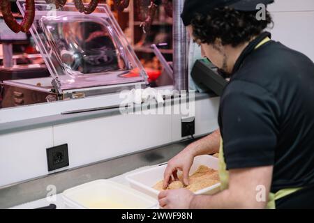 une vue arrière d'un cuisinier panant des nuggets de poulet fraîchement préparés dans la chapelure à sa boucherie. L'attention au détail et le soin dans la préparation est evi Banque D'Images