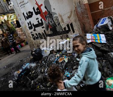 Beyrouth, Liban. 19 mars 2024. Des enfants palestiniens du camp de réfugiés de Shatilla, Beyrouth, Liban, marchent devant une murale représentant la mère du combattant palestinien tué Ibrahim al-Naablusi tenant un M4 lors de ses funérailles en Cisjordanie le 19 mars 2024. Le texte se lit comme suit : « personne ne quitte l’arme ». Le camp de réfugiés de Shatilla abrite environ 30 000 Syriens et Palestiniens déplacés. (Photo de Collin Mayfield/Sipa USA) crédit : Sipa USA/Alamy Live News Banque D'Images