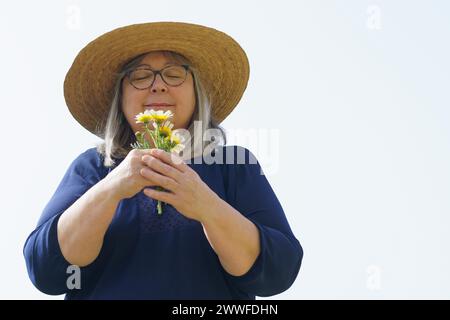 Femme mature souriante avec les cheveux blancs et chapeau avec un bouquet de marguerites dans ses mains isolé sur un fond blanc Banque D'Images