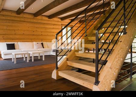 Escaliers en bois avec balustrades en fer forgé noir et canapés rembourrés de tissu de coton blanc dans le salon à l'intérieur de la maison en bois de style contemporain Banque D'Images