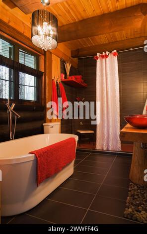 Baignoire autoportante blanche, cabine de douche et lavabos de bol rouge dans la salle de bain principale à l'intérieur de la maison en rondins de style contemporain, Québec, Canada Banque D'Images