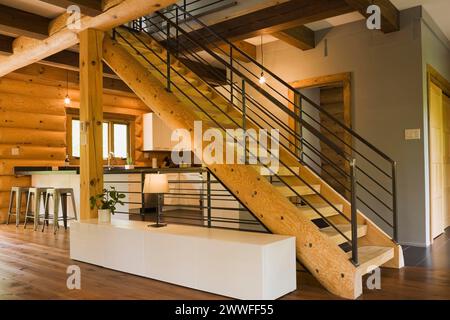 Cuisine avec armoires en bois blanc, tabourets de bar en métal et escaliers en bois avec balustrades en fer forgé noir et longue table d'armoire à l'intérieur Banque D'Images