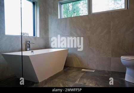 Baignoire blanche autoportante en forme de récipient dans la salle de bains avec carrelage en céramique grise et murs au rez-de-chaussée dans la maison moderne de style cubiste, Québec Banque D'Images