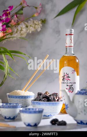 Service à thé asiatique aux motifs bleus, une bouteille de vin de prune chinois, des fruits secs et un bol de riz Banque D'Images