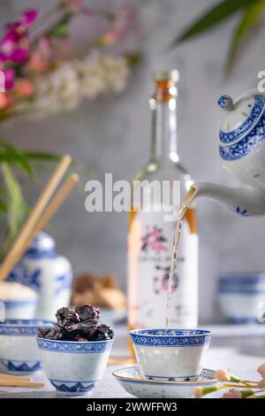 Verser le thé, service de thé asiatique avec des motifs bleus, une bouteille de vin de prune de Chine en arrière-plan, fruits secs Banque D'Images