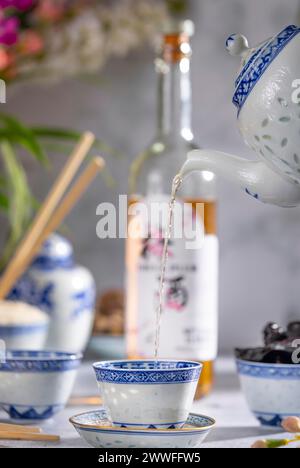 Verser le thé, service de thé asiatique avec des motifs bleus, une bouteille de vin de prune de Chine en arrière-plan, fruits secs Banque D'Images