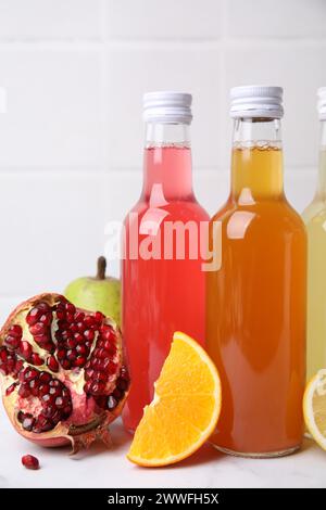 Délicieux kombucha dans des bouteilles en verre et des fruits frais sur une table blanche Banque D'Images