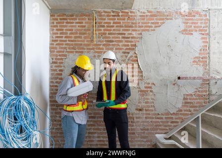 Deux ouvriers de la construction vérifiant l'horaire de travail sur l'ordinateur tablette. Portez un casque de sécurité et un gilet de sécurité, tenez-vous devant un mur de briques sur le chantier de construction. Banque D'Images