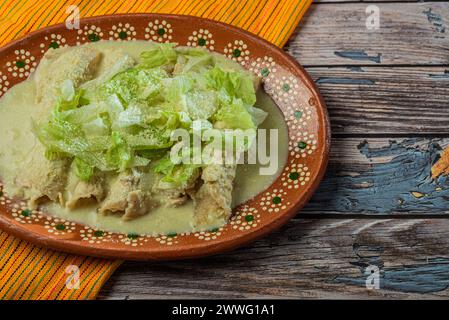 Enchiladas vertes avec de la laitue servie dans un plat en argile sur une table en bois. Banque D'Images