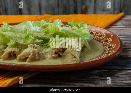 Enchiladas vertes avec de la laitue servie dans un plat en argile sur une table en bois. Banque D'Images