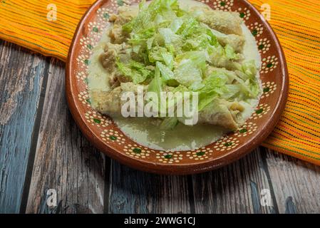 Enchiladas vertes avec de la laitue servie dans un plat en argile sur une table en bois. Banque D'Images