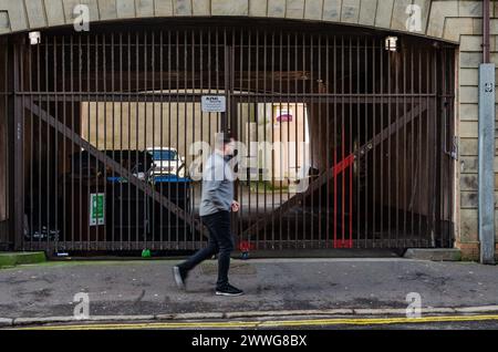 Belfast County Antrim Irlande du Nord 23 février 2024 -Un homme dans un toit gris marchant devant une double porte fermée avec des voitures garées dans une cour Banque D'Images