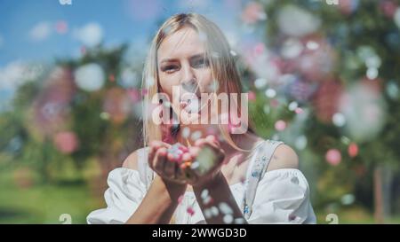 Une fille souffle des confettis en papier multicolores de ses mains. Banque D'Images