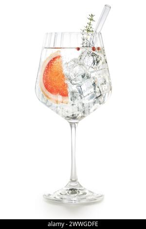Verre ballon ondulé de gin tonic avec pamplemousse, poivre rose, bâton de thym et paille de verre isolé sur fond blanc. Banque D'Images