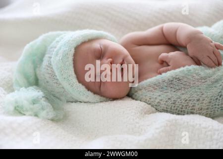 Joli bébé nouveau-né dans un chapeau chaud dormant sur un tissu écossais blanc Banque D'Images