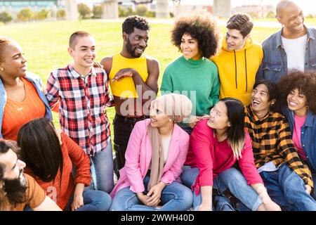 Heureux jeunes gens multiraciaux s'amusant assis sur l'herbe dans un parc public - diversité et concept d'amitié Banque D'Images