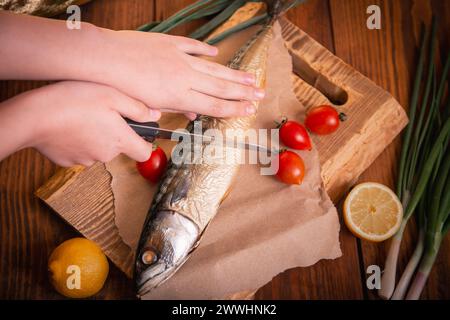 Gros plan de maquereau fumé. Mains femelles coupant le poisson avec un couteau dans la cuisine. Banque D'Images