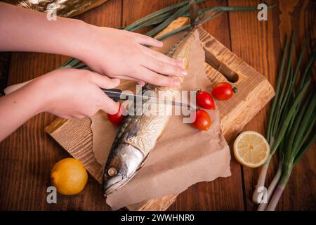 Gros plan de maquereau fumé. Mains femelles coupant le poisson avec un couteau dans la cuisine. Banque D'Images