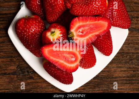 Fraises sur une plaque blanche et fond en bois. Fruits rouges. Alimentation saine. Régime végétalien. Photo Moody de fruits. Banque D'Images
