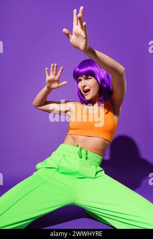 Danseuse femme insouciante portant des vêtements de sport colorés performants sur fond violet danseuse femme active insouciante porter danseuse insouciante Banque D'Images