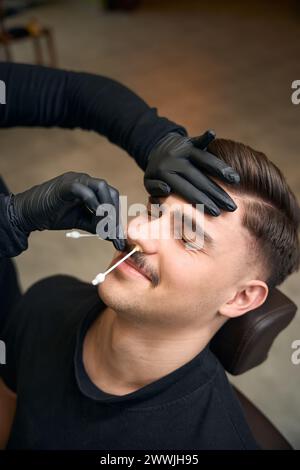 Maître barbier méconnaissable enlève les cheveux du nez de l'homme avec de la cire Banque D'Images