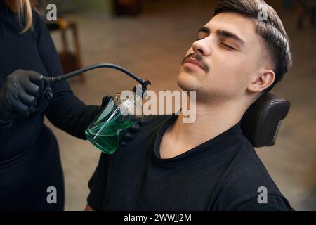 Femme barbier pulvérisant le parfum sur les cheveux du client dans le salon de coiffure Banque D'Images