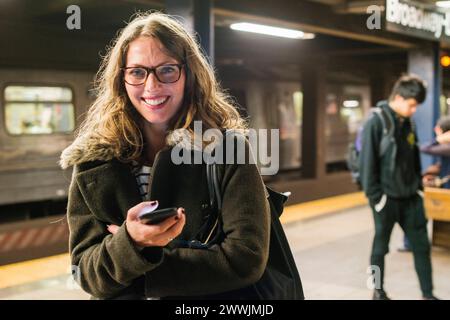 Subway commuter et son smartphone New York City, USA. Blonde, femme banlieue jouant avec son smartphone, en attendant le nouveau train de métro relié à la maison. New York City Subway New York États-Unis d'Amérique Copyright : xGuidoxKoppesx Banque D'Images