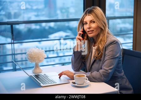 Blonde communique sur son téléphone portable autour d'une tasse de café Banque D'Images