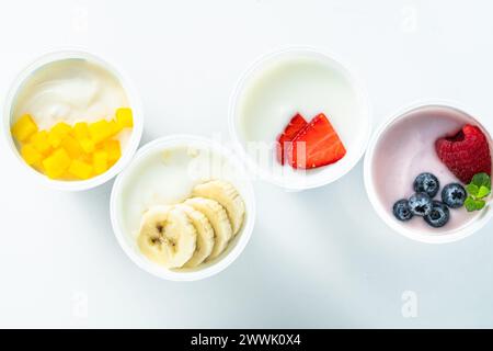 assortiment de différents yaourts avec baies, fruits, mangue et banane sur blanc. petit déjeuner sain Banque D'Images