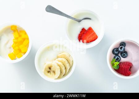 assortiment de différents yaourts avec baies, fruits, mangue et banane sur blanc. petit déjeuner sain Banque D'Images