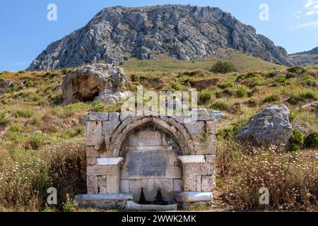 Fontaine médiévale en pierre à la base de la colline Acrocorinthe, dans l'ancienne Corinthe, Grèce. Il a été construit en 1515 et a une inscription ottomane dessus. Banque D'Images