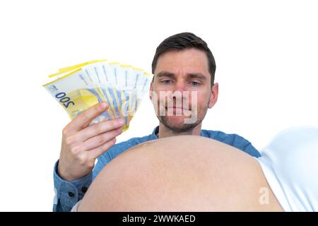 Description : Père-à-être avec des billets de banque à la main contemple la bosse de bébé enceinte réfléchie. Dernier mois de grossesse - semaine 39. Fond blanc. BR Banque D'Images