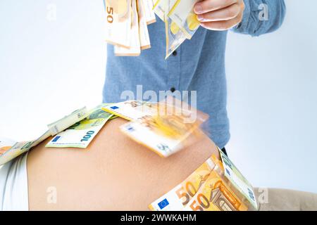 Description : père méconnaissable laisse tomber des billets de banque sur la bosse de bébé enceinte. Dernier mois de grossesse - semaine 39. Fond blanc. Prise de vue brillante. Banque D'Images