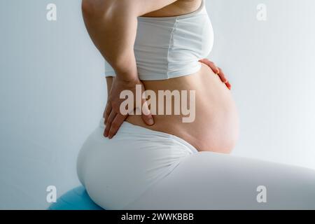 Description : section médiane d'une femme méconnaissable assise sur un ballon de gymnastique et faisant des exercices contre son mal de dos. Vue latérale. Fond blanc. Brig Banque D'Images