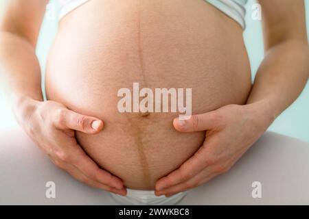 Description : gros plan de la mère et tenant doucement sa bosse de bébé enceinte très ronde. Vue de face. Fond turquoise. Prise de vue brillante. Banque D'Images