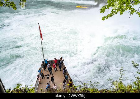 Description : les touristes expérimentent les puissantes cascades à côté du château de Laufen aux chutes du Rhin depuis la plate-forme et les bateaux d'excursion. Chutes du Rhin Banque D'Images