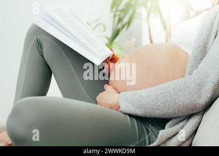 Description : vue de côté de la femme dans les derniers mois de grossesse tenant doucement son ventre tout en lisant un livre. Grossesse troisième trimestre - semaine 34 Banque D'Images