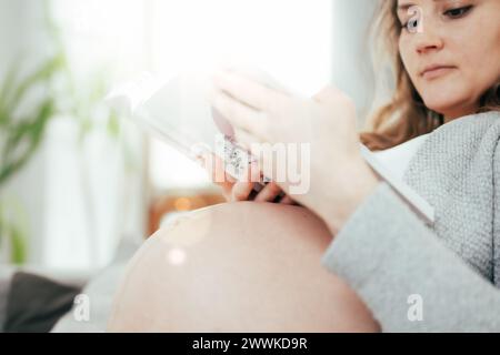 Description : vue de la femme dans les derniers mois de grossesse tenant doucement son ventre tout en lisant un livre. Grossesse troisième trimestre - semaine 34. DSI Banque D'Images