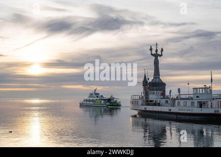 Beschreibung : die Katamaran-Fähre verlässt BEI Sonnenaufgang die Hafeneinfahrt von Konstanz und die Imperia-Statue blickt auf den Horizont mit den sch Banque D'Images