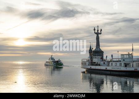 Beschreibung : die Katamaranfähre verlässt BEI Sonnenaufgang die Hafeneinfahrt von Konstanz und die Imperia-Statue blickt in Richtung Horizont mit den Banque D'Images