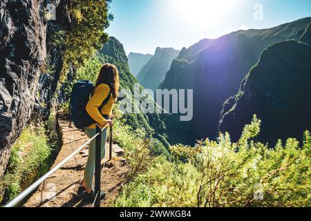 Description: Backpacker femme jouissant d'une vue panoramique depuis le dessous grand mur de roche le long du canal d'eau à la falaise raide à travers la forêt tropicale de Madère. Levada Banque D'Images