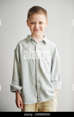 Portrait de garçon heureux dans des vêtements décontractés gardant la main dans la poche. Adorable garçon souriant à la caméra. Enfant élégant posant sur fond blanc. Banque D'Images