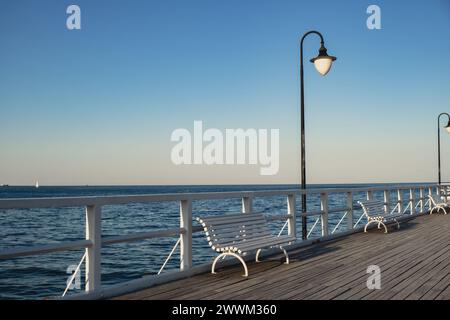 Blanc Vieux ponton de pont en bois contre beau fond naturel de ciel de coucher de soleil, fond d'écran scène de mer polyvalente. Bancs blancs pas de gens à Gdynia Orlowo, Pologne. Jetée en bois, molo avec marina et plage destination touristique Banque D'Images