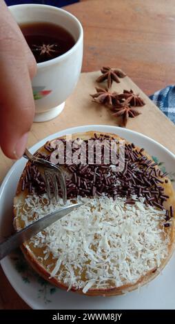 Une photo de quelqu'un mangeant un mini martabak et buvant une tasse de thé sur une table en bois Banque D'Images