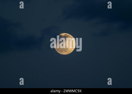 Pleine Lune, ou Worm Moon, le 24 mars 2024 brillant à travers de minces nuages, photographié au-dessus de Londres, Royaume-Uni dans le ciel crépusculaire. Banque D'Images